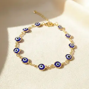 • Gold-toned evil eye link bracelet with round blue charms displayed on an off-white backdrop.