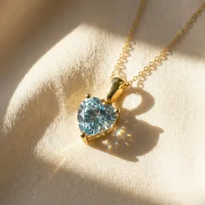 "A delicate gold chain necklace with a heart-shaped, faceted light blue aquamarine gemstone pendant."