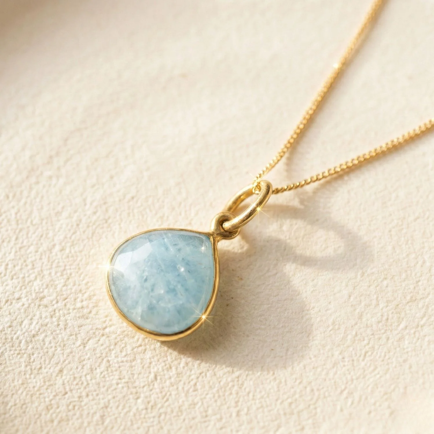 "A delicate gold chain necklace featuring a teardrop-shaped light blue aquamarine gemstone pendant."