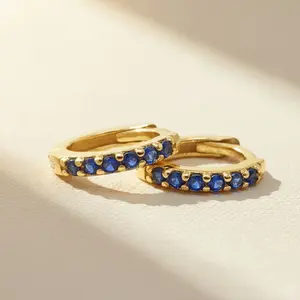 "A pair of small gold huggie hoop earrings lined with a row of round-cut, deep blue sapphire gemstones."
