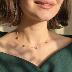 Dainty gold station necklace with multi-colored gemstones worn with an off-the-shoulder green top.