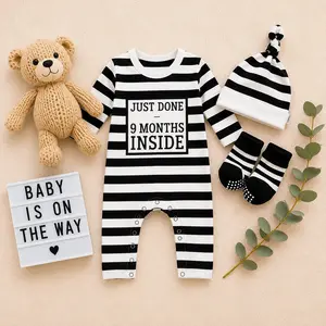 A pregnancy announcement flat lay featuring a black-and-white horizontally striped baby onesie that reads "JUST DONE 9 MONTHS INSIDE," paired with a matching striped knotted hat, striped socks, a small beige teddy bear, and a light box sign reading "BABY IS ON THE WAY."