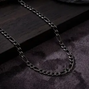 A polished black Figaro chain necklace featuring alternating small round links and longer oval links, displayed on dark wood and plush textured fabric.