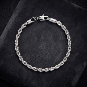 A classic silver rope chain bracelet with a polished lobster clasp, displayed neatly on a dark grey plush fabric backdrop.