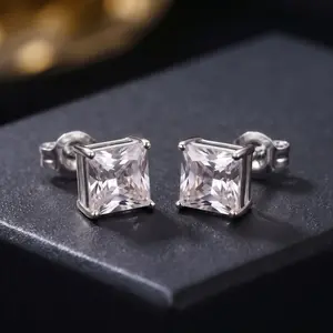 A pair of princess-cut square diamond stud earrings in silver settings resting on a black surface.