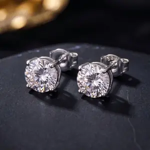 A pair of round-cut diamond stud earrings in silver prong settings resting on a black surface.