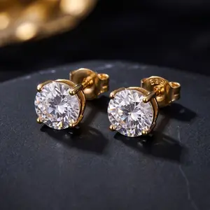 A pair of round-cut diamond stud earrings in yellow gold prong settings resting on a dark surface.