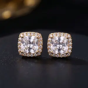 A pair of cushion-cut diamond halo stud earrings in yellow gold settings resting on a dark surface.