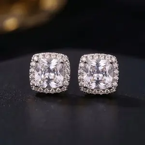 A pair of cushion-cut diamond halo stud earrings in silver settings resting on a dark surface.
