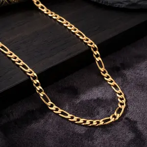 A gold figaro chain necklace draped across a dark wooden block and textured gray surface.