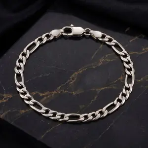 A silver figaro chain bracelet laid flat on a dark marble surface with gold veins.
