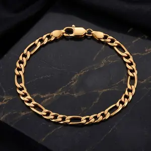A gold figaro chain bracelet laid flat on a dark marble surface with gold veins.