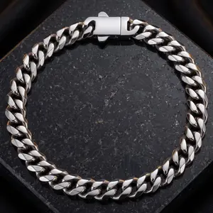 A silver Cuban link chain bracelet laid flat in a circular arrangement on a speckled dark stone surface.