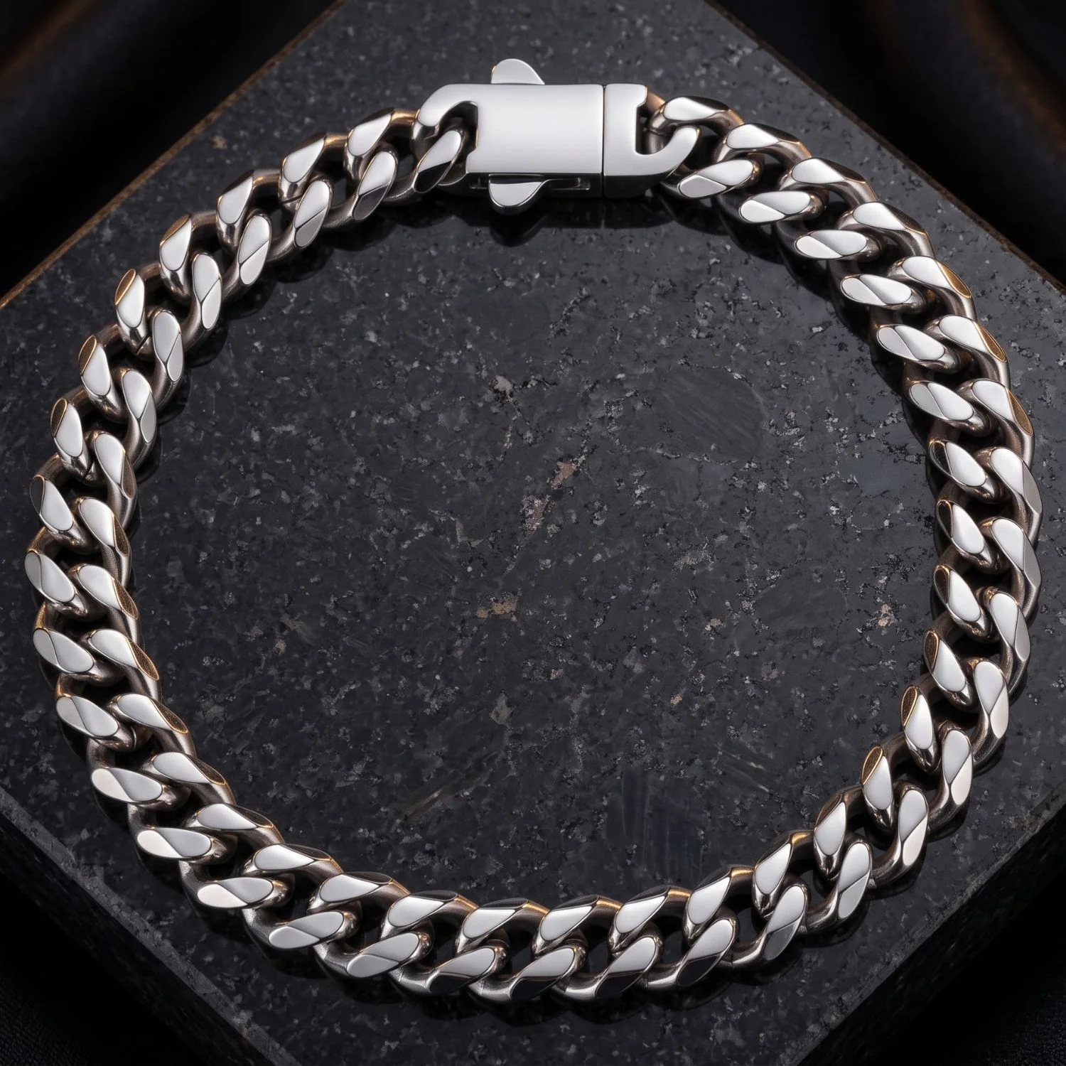 A silver Cuban link chain bracelet laid flat in a circular arrangement on a speckled dark stone surface.