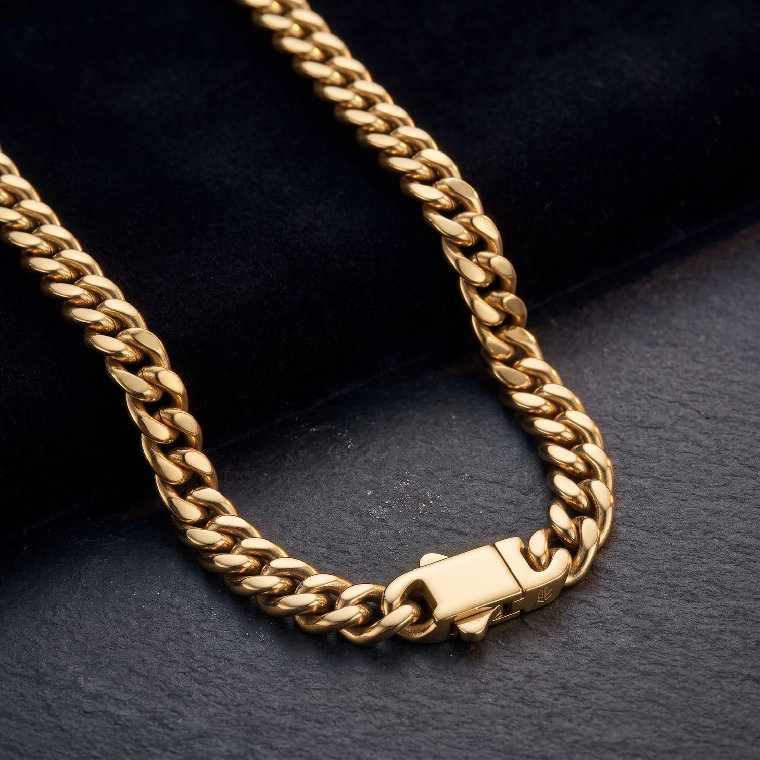 A men's thick gold Cuban link chain necklace featuring a modern rectangle box clasp, displayed on black velvet and dark slate.