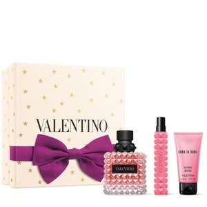 Valentino Donna Born In Roma fragrance gift set featuring a cream box decorated with gold stars and a large purple bow, alongside a rockstud-textured perfume bottle, a matching travel spray, and a pink tube of body lotion.